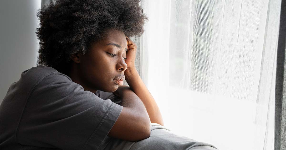O que pode agravar a depressão resistente? 1 Pessoa pensativa apoiada na janela, representando os fatores que podem agravar a depressão resistente